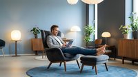 Relaxed businessman reading book in modern living room with mid-century furniture, warm lighting and plants creating cozy atmosphere for home office design.