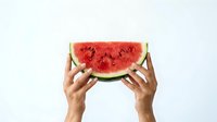 Hands holding fresh watermelon slice with red flesh and green rind against white background, suitable for food, summer, and healthy eating designs.