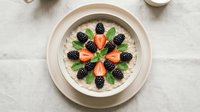 Creamy yogurt bowl topped with fresh blackberries, strawberries, and mint leaves arranged in a decorative pattern on white marble surface.