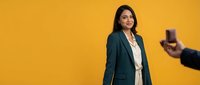 Professional businesswoman in teal blazer posing confidently against vibrant yellow background for corporate photography and marketing materials.