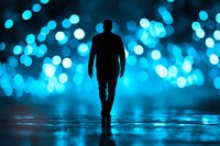 Silhouette of man walking alone on wet reflective surface against bright blue bokeh lights background, creating mysterious atmospheric night scene.