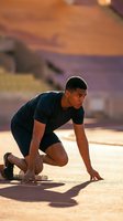 Athletic young African American man in starting position ready to sprint on urban street during golden hour sunset with warm lighting and city backdrop.