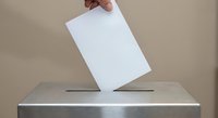 Hand placing white ballot paper into metal voting box during election process for democratic participation and civic duty.