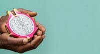 Hands holding fresh cut dragon fruit with white flesh and black seeds against turquoise background for food and wellness content.