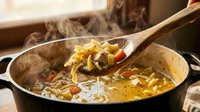 Hot noodle soup with vegetables steaming in cast iron pot, wooden spoon lifting noodles, Asian cuisine cooking preparation.