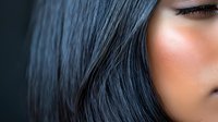 Close up portrait of young Asian woman with long dark hair and natural makeup against dark background, showing partial face with focus on eye area.