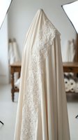 Elegant cream-colored bridal gown with intricate lace detailing along the bodice and flowing fabric, displayed on mannequin in bright studio setting for wedding fashion design.