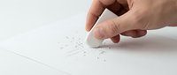 Hand holding white eraser removing pencil marks from paper, creating eraser shavings. Mistake correction, editing, learning concept for education materials.