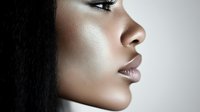 Close-up profile portrait of young African American woman with flawless glowing skin and natural makeup looking away with serene expression against soft background.