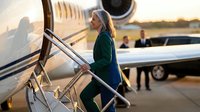 Professional blonde businesswoman in green suit boarding private jet at sunset for luxury corporate travel and executive transportation.