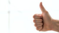 Hand showing thumbs up gesture against blurred background expressing approval, success and positive feedback for business and communication concepts.
