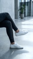 Woman legs in gray leggings and white sneakers sitting in modern office lobby with concrete floor and glass walls for lifestyle and fashion concepts.