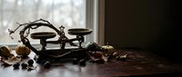 Vintage brass balance scale with weights on wooden table surrounded by autumn leaves near window creating rustic antique atmosphere for home decor.