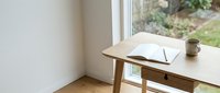 Minimalist wooden desk with open notebook and coffee mug by window overlooking garden, creating peaceful home office workspace for productivity and focus.
