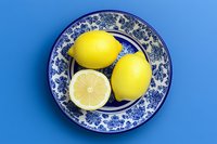Fresh yellow lemons on a blue and white floral ceramic plate against a vibrant blue background, top view, healthy food concept.