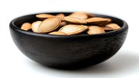 Roasted pumpkin seeds in black wooden bowl on white background, nutritious snack rich in minerals and vitamins.