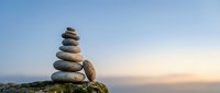 Balanced stone cairn stack on rocky surface against serene sunset sky, symbolizing harmony, meditation, mindfulness and spiritual wellness practices.