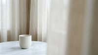 White ceramic mug on marble table with sheer curtains in background, isolated on neutral setting for product mockup and branding designs.