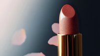 Luxurious rose gold metallic lipstick close-up on dark background with soft bokeh lights. Elegant cosmetic product photography highlighting shimmer and texture.
