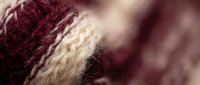 Soft burgundy and cream wool yarn texture with intricate knitted pattern detail for cozy winter crafts and handmade textile projects.