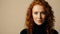 Professional redhead woman with curly hair in black turtleneck against neutral background for business and corporate marketing materials.