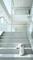 White sneakers on modern marble staircase in contemporary home with glass railings and natural light creating minimalist architectural interior design.