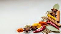 Aromatic spices and herbs scattered on neutral background with cinnamon sticks, star anise, turmeric, paprika and bay leaves for culinary cooking.