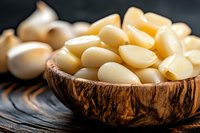 Peeled garlic cloves in rustic wooden bowl on dark surface. Fresh organic ingredients for cooking and culinary preparations in kitchen setting.
