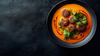 Delicious meatballs in rich tomato sauce garnished with fresh herbs served in black bowl on dark textured background for culinary presentations.