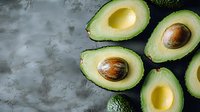 Halved avocados with pits displayed on gray textured surface, suitable for food photography, healthy eating content, recipe blogs, and culinary design projects.