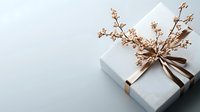 Elegant white gift box decorated with golden ribbon bow and delicate dried flowers on light gray background, minimalist festive composition.