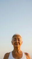 Senior woman with short white hair and East Asian ethnicity, wearing a white sleeveless top, smiling outdoors against a clear sky. Portrait suitable for wellness, aging, health and lifestyle content.
