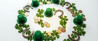 St. Patrick's Day festive arrangement with green leprechaun hats, golden coins, horseshoes and shamrock clovers forming decorative circles on white background.