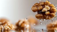 Fresh walnut kernel with water droplets splashing around it on neutral background for healthy snacking and cooking ingredients.