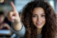Young Hispanic woman with curly dark hair and bright smile pointing forward with index finger. Casual style portrait showing confidence and positive attitude.