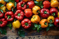 Fresh red, yellow and orange bell peppers with green leaves scattered on rustic wooden background, colorful healthy organic vegetables arranged in rows.