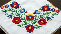 Traditional folk embroidery with colorful floral motifs on white fabric corner, featuring red roses and blue flowers with green leaves in ethnic style.