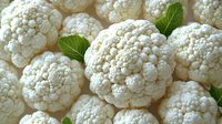 Fresh white cauliflower heads with bright green leaves arranged in pattern, macro view. Raw organic vegetables background for healthy eating and cooking.