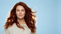 Young Caucasian woman with flowing red hair in white shirt against blue background for beauty and lifestyle advertising campaigns.