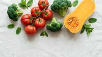Fresh organic vegetables including ripe red tomatoes, green broccoli, butternut squash and basil leaves arranged on white wooden background for healthy cooking.