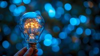 Glowing light bulb with warm filament held in hand against blue bokeh background representing innovation, creativity, and bright ideas for business concepts.