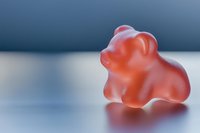 Single red gummy bear candy closeup on reflective surface with soft blue background, shallow depth of field, sweet treat concept.