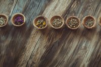 Aromatic dried herbs and flower petals in wooden bowls arranged in row on rustic wooden table background, natural wellness and alternative medicine concept.