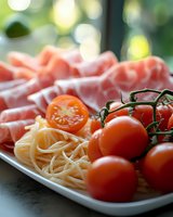 Fresh pasta with cherry tomatoes and cured meat on white plate, outdoor dining setup with natural bokeh background for culinary and food photography projects.