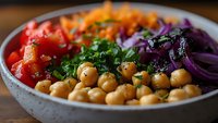 Colorful healthy Buddha bowl with chickpeas, fresh vegetables, red cabbage, carrots, and herbs on wooden table for nutritious meal planning.