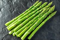 Fresh green asparagus spears arranged on dark stone background, raw organic vegetables for healthy cooking and seasonal spring menu preparation.