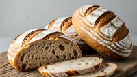 Freshly baked artisan sourdough bread loaves with golden crust and airy crumb texture on wooden cutting board, perfect for bakery marketing materials.