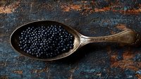 Fresh black peppercorns in vintage silver spoon on dark rustic wooden background with copy space. Food photography for culinary blogs and recipes.