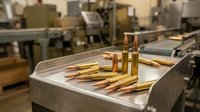 Brass ammunition cartridges on industrial conveyor belt in manufacturing facility. Production line for military or hunting bullets in factory setting.