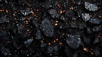 Black coal pieces with water drops and glowing embers scattered on dark background, creating dramatic contrast between wet surface and burning particles.